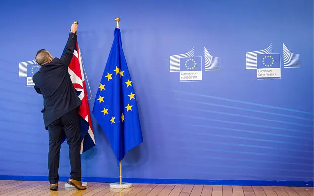 An EU official hangs the Union Jack next to the European Union flag at the VIP entrance at the European Commission headquarters in Brussels on Tuesday, Feb. 16, 2016. British Prime Minister David Cameron is visiting EU leaders two days ahead of a crucial EU summit.  (AP Photo/Geert Vanden Wijngaert)