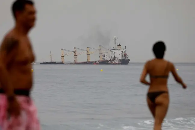 Dos personas pasean en la playa de Levante con el 'OS 35' al fondo