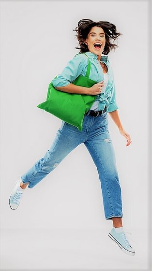 consumerism, sustainability and people concept - portrait of happy smiling young woman in turquoise shirt and jeans walking with green reusable canvas bag for food shopping over grey background