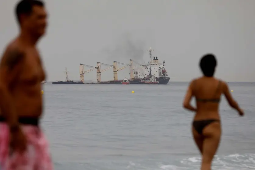 Dos personas pasean en la playa de Levante con el 'OS 35' al fondo